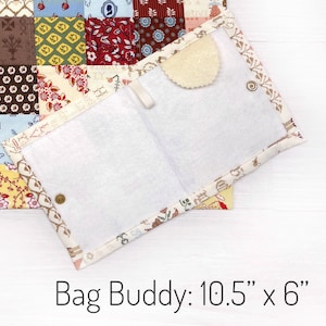 May include: Open, quilted fabric Bag Buddy, measuring 10.5" x 6", with a white interior and a beige, patterned border. The Bag Buddy has a snap closure and a small, round, beige felt piece. The background features a patchwork quilt.