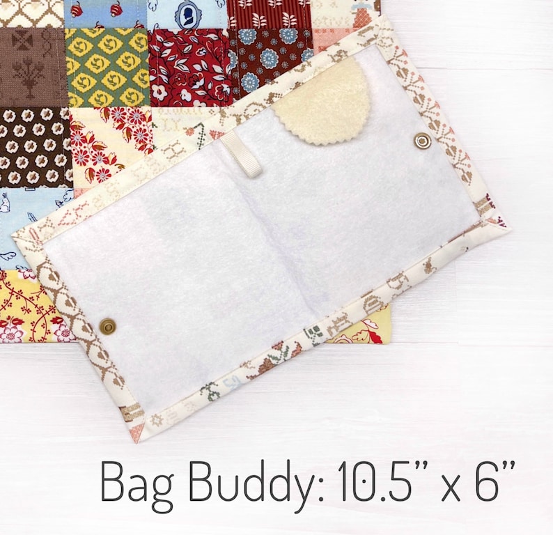 May include: Open, quilted fabric Bag Buddy, measuring 10.5" x 6", with a white interior and a beige, patterned border. The Bag Buddy has a snap closure and a small, round, beige felt piece. The background features a patchwork quilt.