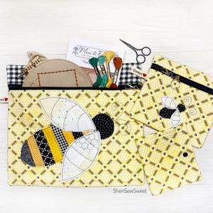May include: A set of three zippered pouches with a honeycomb pattern and a bee applique. The pouches are made of yellow fabric with black accents. The largest pouch has a larger bee applique with a black and yellow striped body. The pouches are perfect for storing small items like sewing supplies or jewelry.