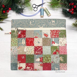 May include: A square fabric pouch featuring a patchwork design of various holiday-themed patterns in red, green, and cream. The pouch has a top zipper with a metal ring pull and a small white tag labeled Sweet with a red heart icon.