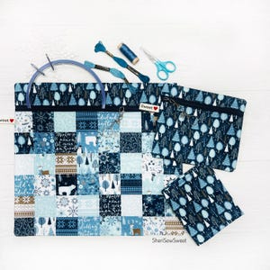 May include: A patchwork tote bag, two zippered pouches, and a small square pouch. The bags feature a winter-themed pattern in shades of blue and white. Embroidery floss, scissors, and a blue embroidery hoop are also present.