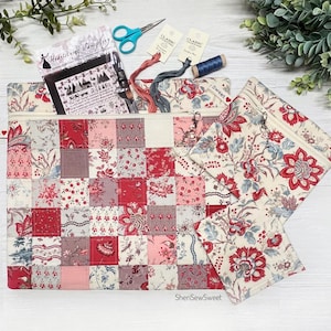May include: A patchwork zippered pouch and matching small pouch with floral patterns in red, pink, and cream. The larger pouch contains embroidery supplies, including scissors, thread, and a needlepoint pattern. The word "Sweet" is on a tag.