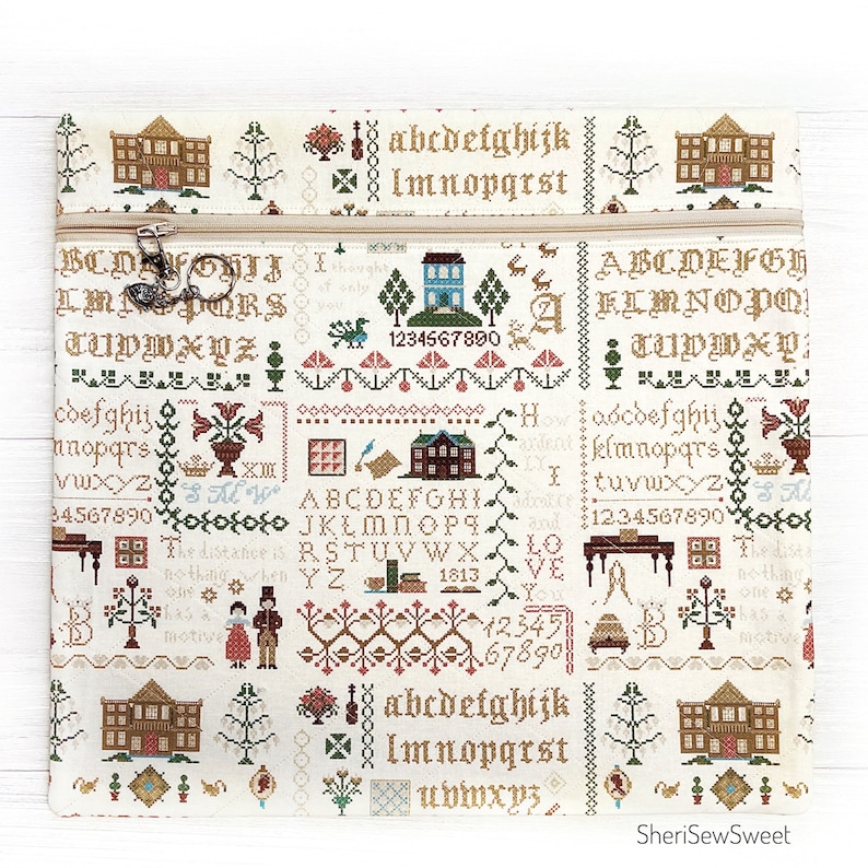 May include: Cream-colored zippered pouch with a cross-stitch design featuring houses, trees, and alphabet letters in brown, green, and red. The text "SheriSewSweet" is at the bottom.