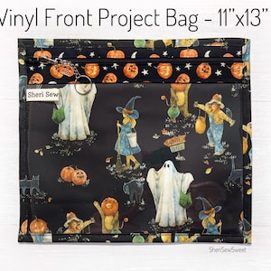 May include: A black vinyl project bag with a Halloween-themed design. The bag features a clear front panel with illustrations of ghosts, witches, pumpkins, and other spooky characters. The bag measures 11" x 13" and has a zipper closure.