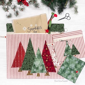 May include: A collection of Christmas-themed fabric pouches and accessories. The main pouch features red and white striped fabric with appliqued Christmas trees. Other items include a small zippered pouch, a tree-shaped charm, and a snowflake-patterned square. The text "Snowballs for" is visible.