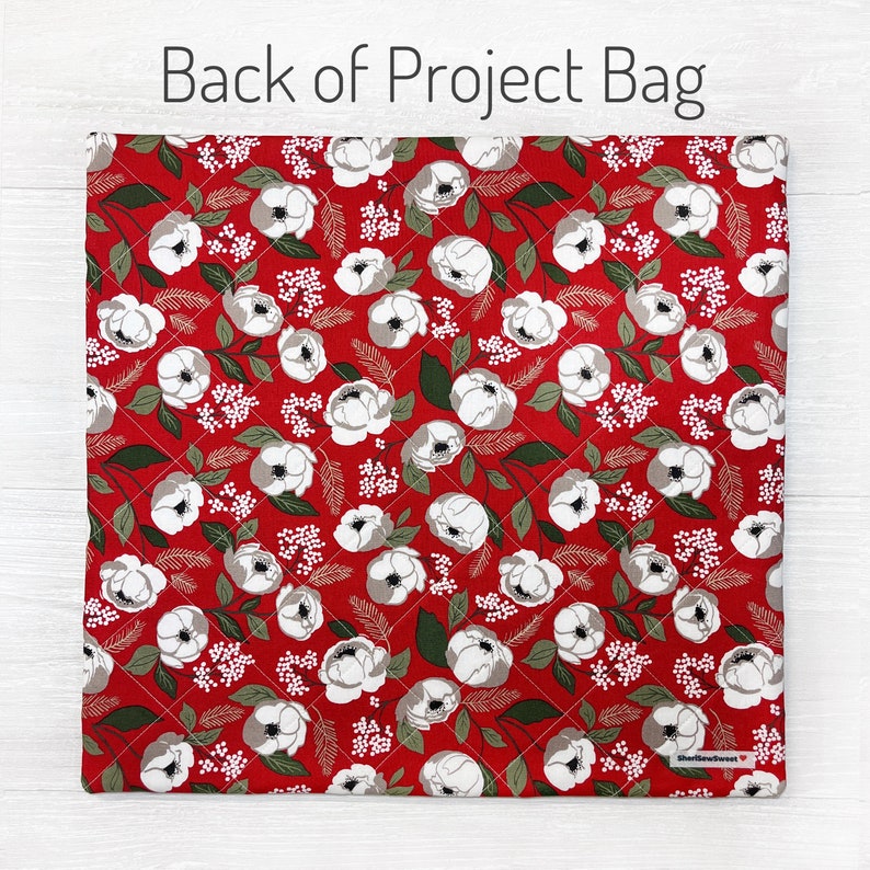 K&ouml;nnte beinhalten: Roter, gesteppter Projektbeutel mit floralem Muster. Das Design zeigt wei&szlig;e und graue Blumen, gr&uuml;ne Bl&auml;tter und kleine wei&szlig;e florale Akzente. Der Text "Back of Project Bag" steht oben.
