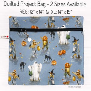 May include: Quilted project bag with a Halloween theme. The bag is light blue with a repeating pattern of ghosts, pumpkins, black cats, and costumed figures. The bag has a black zipper and a small charm. The text on the bag reads "Quilted Project Bag - 2 Sizes Available" and "REG: 12" x 14" & XL: 14" x 15".