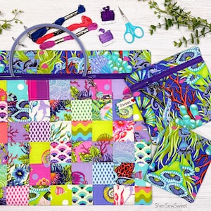 May include: A large zippered project bag and two smaller matching pouches featuring a colorful patchwork of aquatic-themed fabrics with coral, fish, and seaweed patterns. Includes a purple embroidery hoop, embroidery floss, and blue scissors.