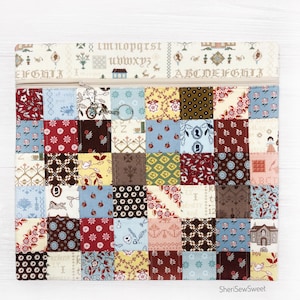 May include: A patchwork zippered pouch with a cream-colored top featuring embroidered letters and floral patterns. The main body is a grid of small, colorful squares with various vintage-style designs. A silver-toned zipper and key ring complete the design.