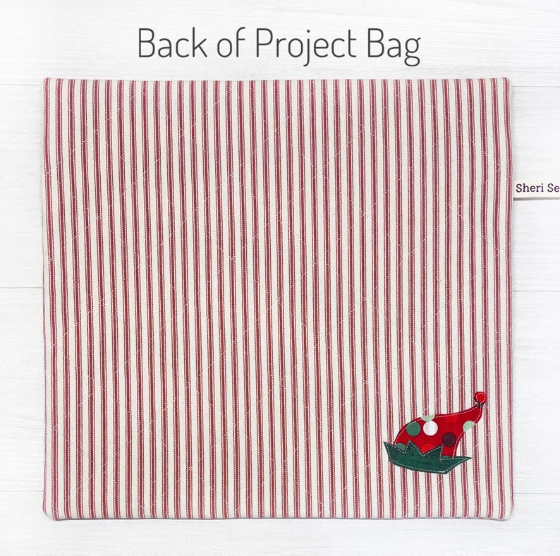May include: Red and white striped fabric project bag with a green and red elf hat applique. The bag has a label that says "Sheri Se".