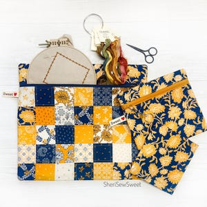 May include: Two fabric zippered pouches with a patchwork design in shades of blue and yellow. The pouches are decorated with a floral pattern and the words "Sweet" are printed on the pouches.