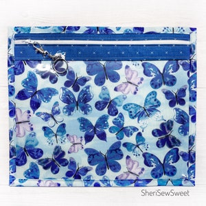 May include: A blue zippered pouch with a clear plastic front featuring a butterfly print. The pouch has a silver key ring attached to the zipper.