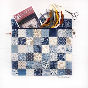 May include: A patchwork fabric project bag with a blue floral pattern. The bag contains a cross-stitch pattern book, embroidery floss, a hoop, and small scissors. The bag has a zipper closure and a small charm. The text "Sweet" is visible.