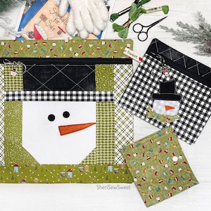 May include: A collection of handmade fabric pouches and accessories with a winter theme. The main pouch features a snowman design with a white face, black eyes, and an orange carrot nose. The pouches are in green and black patterns.