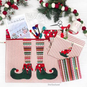 May include: A set of three Christmas-themed zippered pouches with red and white striped fabric. The largest pouch features a green elf's legs and shoes. The smaller pouches feature a red and white striped fabric with a green elf hat design. The pouches are labeled "Sweet".