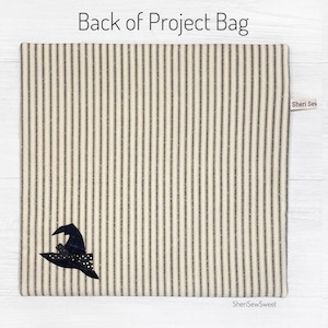 May include: The back of a black and white striped fabric project bag with a black witch hat with gold glitter accents. The bag has a label that says "Sheri Sew Sweet".