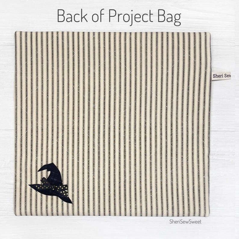 May include: The back of a black and white striped fabric project bag with a black witch hat with gold glitter accents. The bag has a label that says "Sheri Sew Sweet".