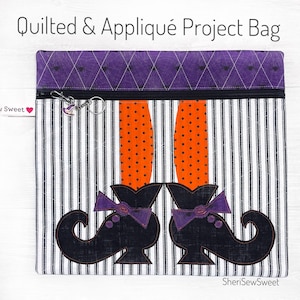 May include: A quilted project bag with a zipper closure and a witch's legs and shoes applique. The bag is made of black and white striped fabric with a purple quilted top. The text "SheriSewSweet" is printed on the bottom right corner of the bag.