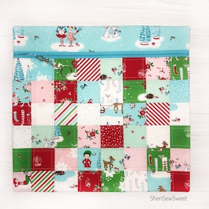 May include: A blue zippered pouch with a patchwork design featuring a variety of Christmas-themed patterns, including elves, reindeer, and snowflakes. The pouch has a zipper closure and a key ring.