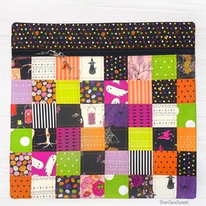 May include: A black zippered pouch with a patchwork design featuring various Halloween-themed fabrics. The fabrics include ghosts, pumpkins, candy corn, and bats. The pouch has a black zipper and a black and white polka dot trim.