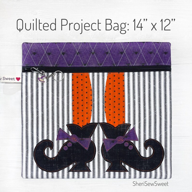 May include: A quilted project bag with a witch's legs and shoes design. The bag is 14 inches by 12 inches and has a black and white striped fabric with orange and black polka dots. The bag has a purple zipper and a purple and black spiderweb design on the top flap.
