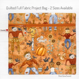 May include: A quilted fabric project bag with a zipper closure. The bag features a colorful autumn-themed print with scarecrows, pumpkins, squirrels, and sunflowers on an orange background. The text "OCTOBER" is visible on the bag.