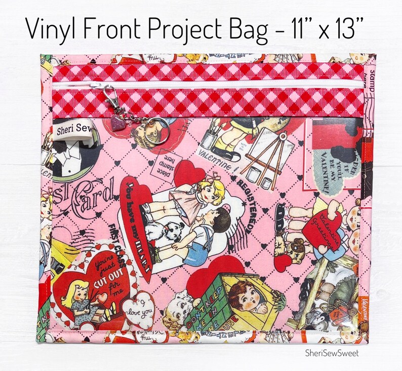 May include: A pink vinyl project bag with a red and white checkered zipper closure. The bag is 11 inches by 13 inches and features a Valentine's Day themed print with hearts, children, and the text "You're just cut out for me".