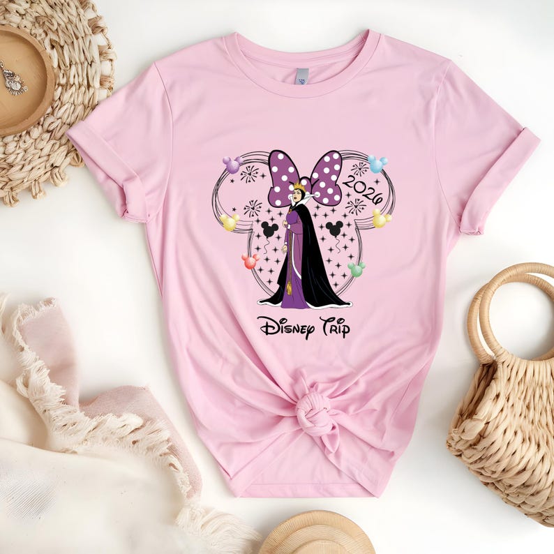 May include: A light pink t-shirt featuring a graphic of a Disney character with a purple bow, the text "2020", and the words "Disney Trip". The design includes black Mickey Mouse silhouettes and colorful balloons.