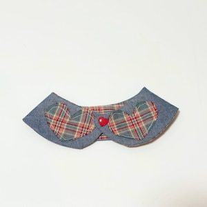 Può includere: Un collare per animali domestici in stile denim con due applicazioni a forma di cuore a quadri e un piccolo bottone a forma di cuore rosso. Il collare ha una base in denim blu e uno sfondo bianco.