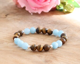 May include: A beaded bracelet featuring alternating light blue and brown tiger eye beads. The bracelet is displayed on a wooden surface with a pink rose in the background. The beads are approximately 0.8 cm in diameter.