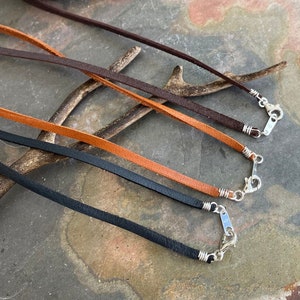 May include: Four leather cords with silver clasps. The cords are brown, orange, black, and dark brown. The cords are arranged in a row, with the brown cord at the top and the dark brown cord at the bottom.