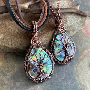 May include: Two copper wire wrapped pendants with abalone shell tree of life designs. The pendants are hanging from leather cords and a silver chain.