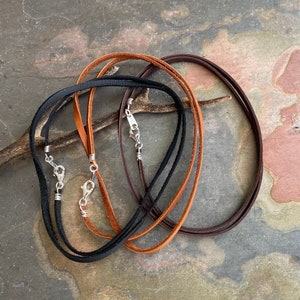 May include: Three leather cords with silver clasps. The cords are brown, black, and a lighter brown color.