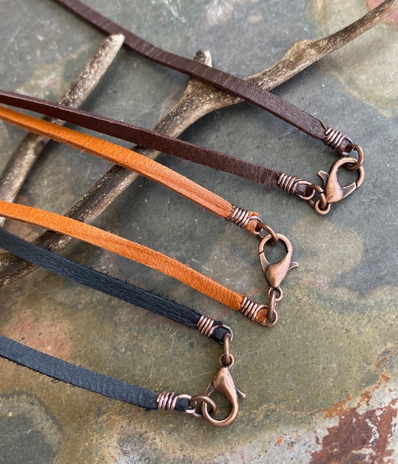 May include: Three leather cords with copper clasps. The cords are brown, orange, and black.