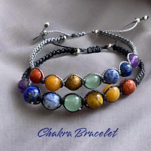 May include: A chakra bracelet with seven colorful beads, including amethyst, lapis lazuli, sodalite, aventurine, tiger's eye, carnelian, and red jasper. The bracelet is made with black and gray string.