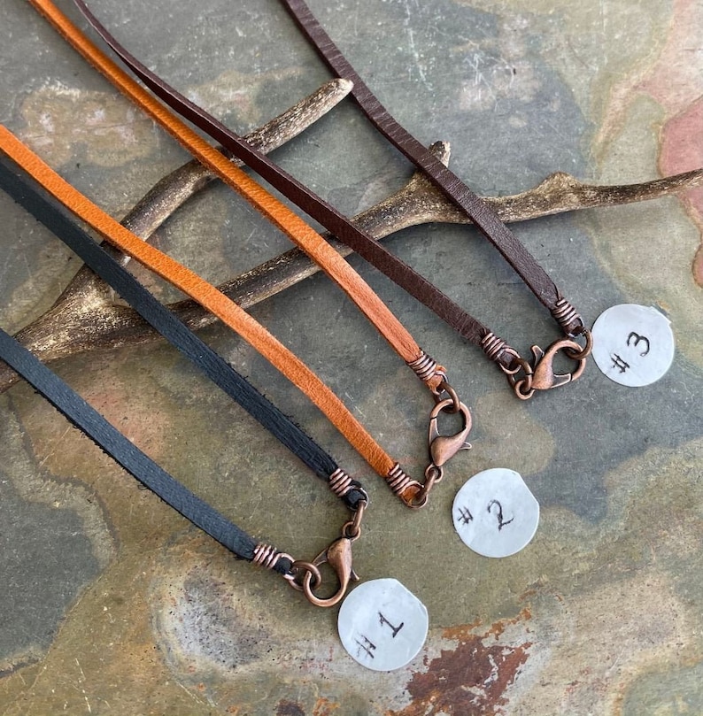 May include: Three leather cords with copper clasps and numbered tags. The cords are brown, tan, and black.