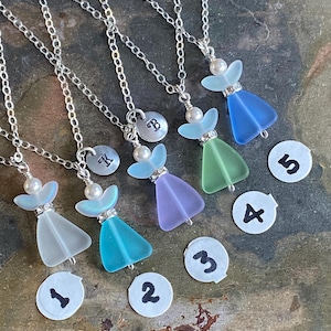 Puede incluir: Cinco collares con forma de &aacute;ngel con cadenas plateadas. Cada collar presenta un colgante de cristal de colores, una perla y un peque&ntilde;o dije plateado. Los colgantes son en tonos azules, verdes y morados. Cada collar tiene un n&uacute;mero en un peque&ntilde;o c&iacute;rculo blanco.