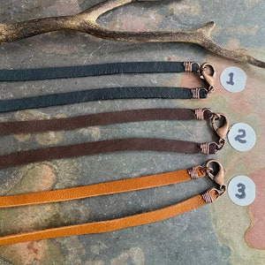 May include: Three leather cords with metal clasps. The cords are black, brown, and tan. The cords are numbered 1, 2, and 3.