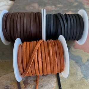 May include: Three spools of leather cord in brown, black, and tan. The cords are wound around white plastic spools.