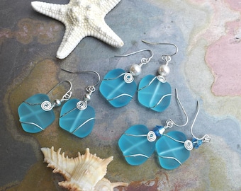 May include: A pair of earrings with blue glass squares wrapped in silver wire. The earrings have a pearl and a blue crystal accent.