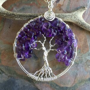 May include: A silver wire wrapped tree of life pendant with amethyst stones. The pendant is round and has a detailed wire design.