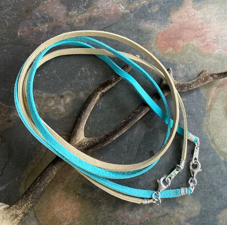 May include: A turquoise and beige leather cord necklace with silver clasps. The cord is wrapped around a branch.