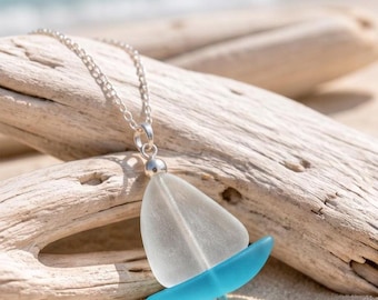 Peut inclure: Un collier à chaîne en argent avec un pendentif en forme de voilier. Le voilier se compose d'une voile en verre dépoli blanc et d'une coque en verre bleu turquoise vif, reliées par une petite bélière en métal argenté au sommet de la voile.