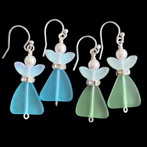 May include: Four pairs of handmade angel earrings. Each earring features a sea glass body in shades of blue and green, with a pearl head and silver-tone hook. A sparkling band accents the waist.