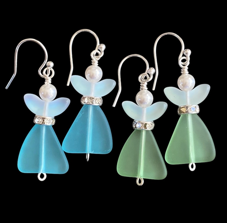 May include: Four pairs of handmade angel earrings. Each earring features a sea glass body in shades of blue and green, with a pearl head and silver-tone hook. A sparkling band accents the waist.