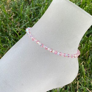 May include: A delicate pink and clear crystal anklet with a shimmering finish. The anklet is made of small, faceted beads and is strung on a thin, clear thread.