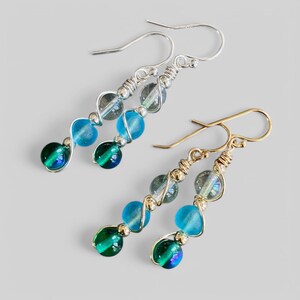 May include: A pair of dangle earrings with blue and green iridescent glass beads. The earrings are made with silver and gold wire.