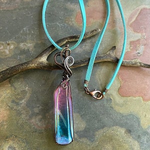 May include: A iridescent crystal pendant wrapped in copper wire, hanging from a turquoise suede cord.