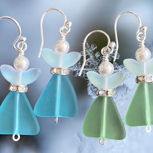 May include: Four pairs of handmade angel earrings. Each earring features a silver hook, a pearl bead, and a decorative crystal band. The angel wings are a light blue or green color, and the body is a matching triangular shape.