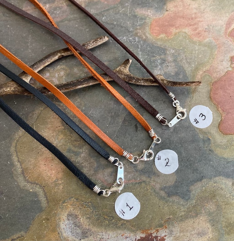 May include: Three leather cords with silver clasps. The cords are black, brown, and orange. Each cord is labeled with a number, #1, #2, and #3.